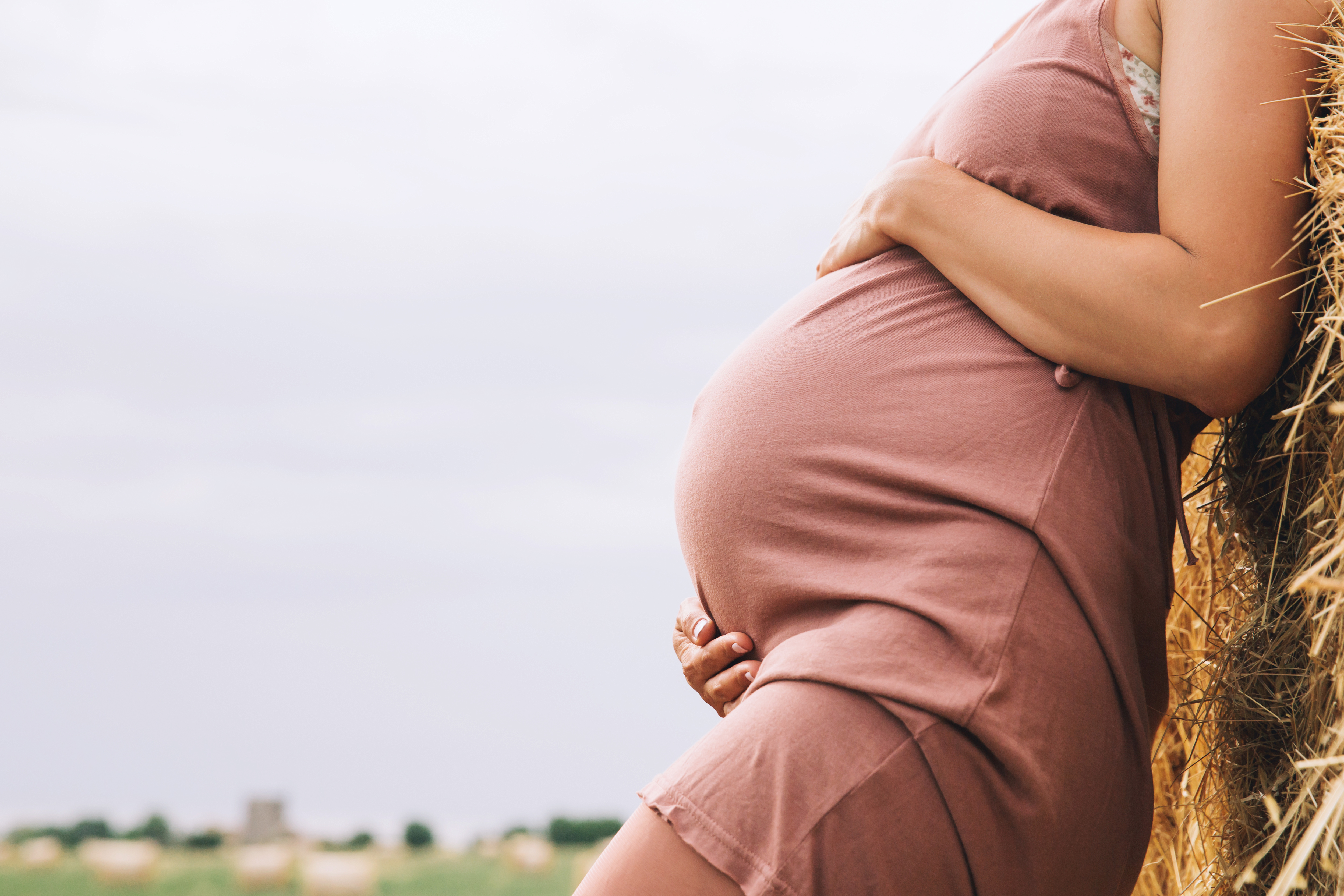 A pregnant woman holding her belly outdoors in natural light